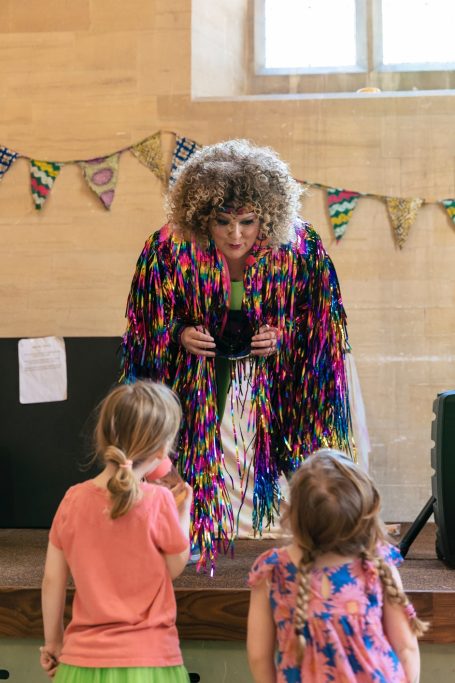 Woman in sparkly jacket inthralls two small children at a party